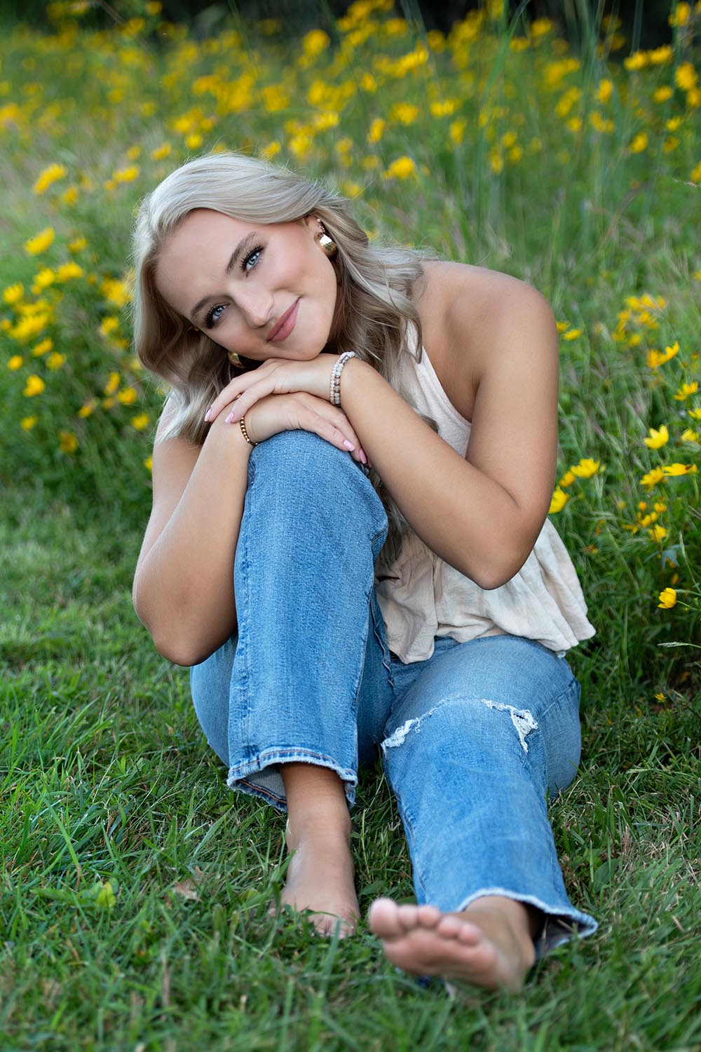 a high school senior girl sitting in grass with yellow flowers.