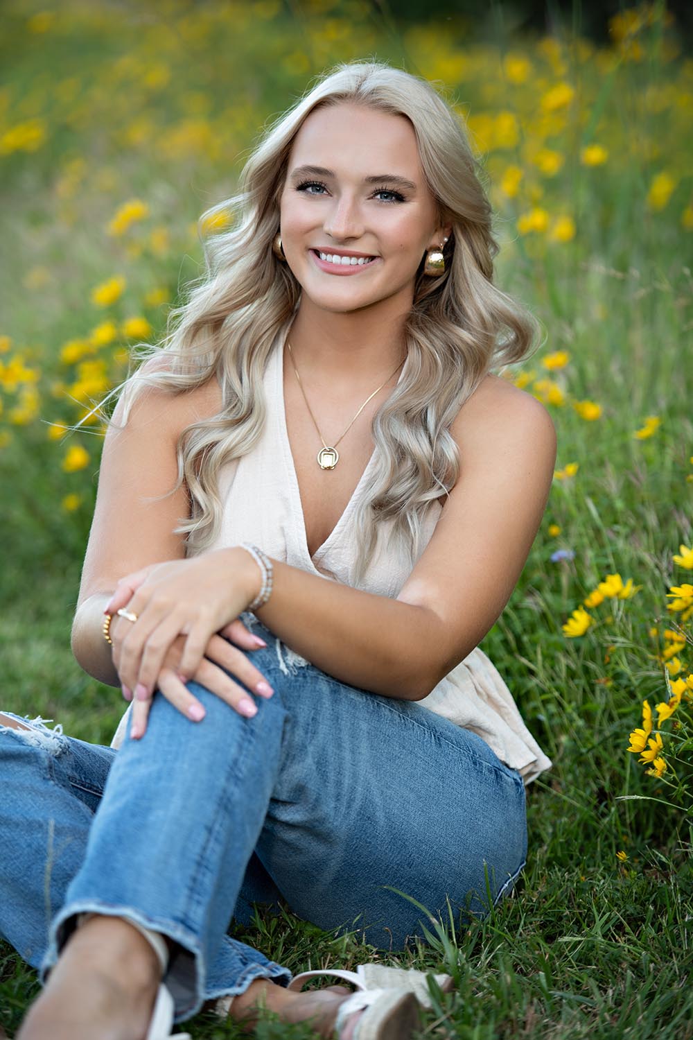 A high school senior girl sitting in grass and yellow flowers.