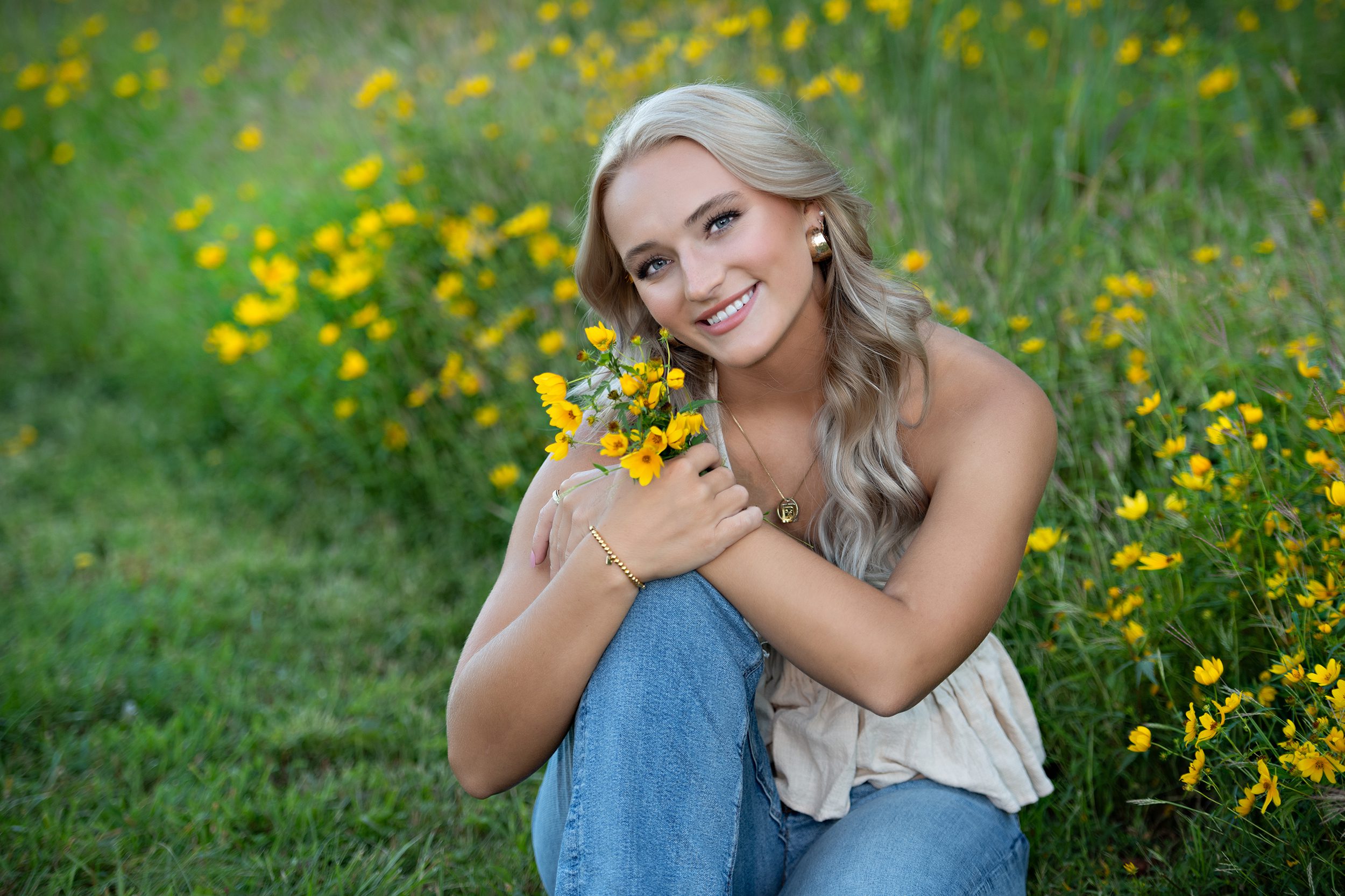 A high school senior girl sitting and holing yellow flowers.